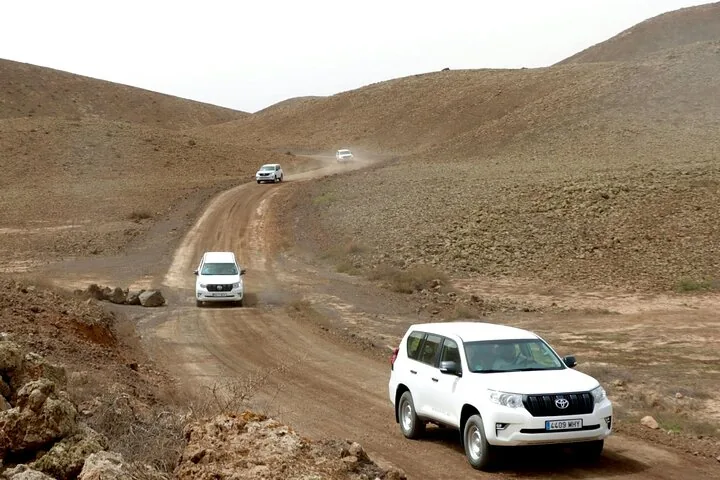 Weiße Geländewagen auf einer Schotterpiste durch eine karge Landschaft