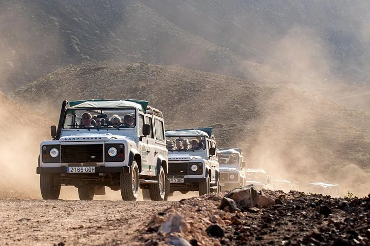 File de Land Rover soulevant la poussière sur une route de terre accidentée