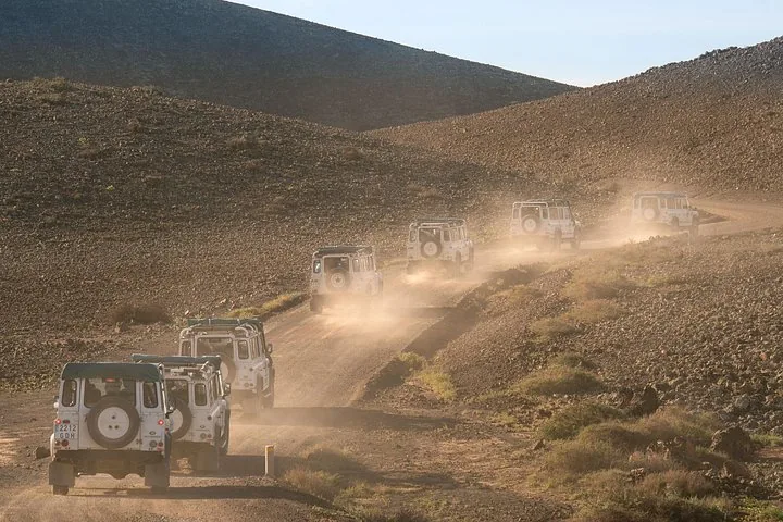 Convoi de véhicules tout-terrain blancs s'éloignant sur une piste poussiéreuse