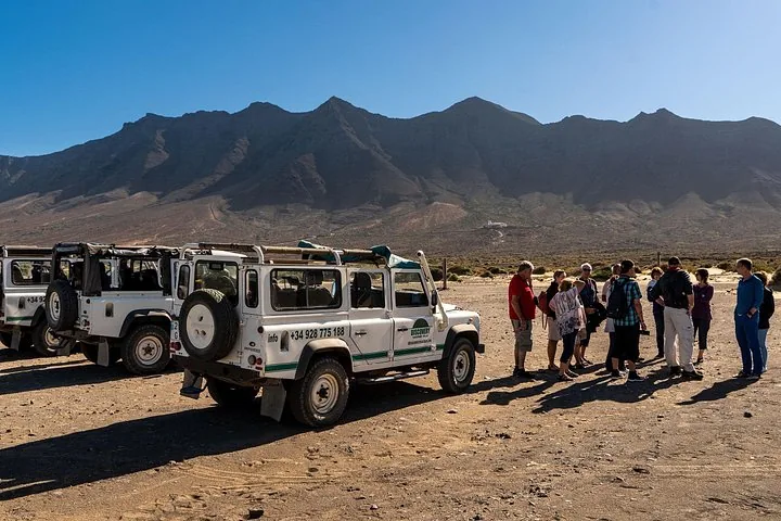 Gruppe von Touristen neben geparkten Land Rovern, dahinter Berge