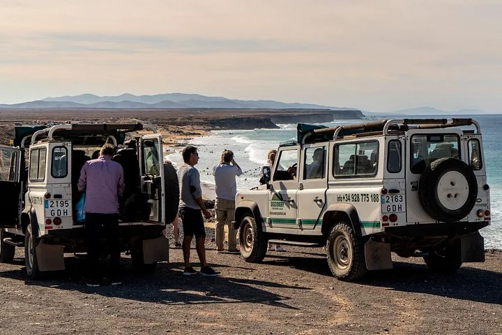Tourists standing near parked Land Rovers overlooking the ocean